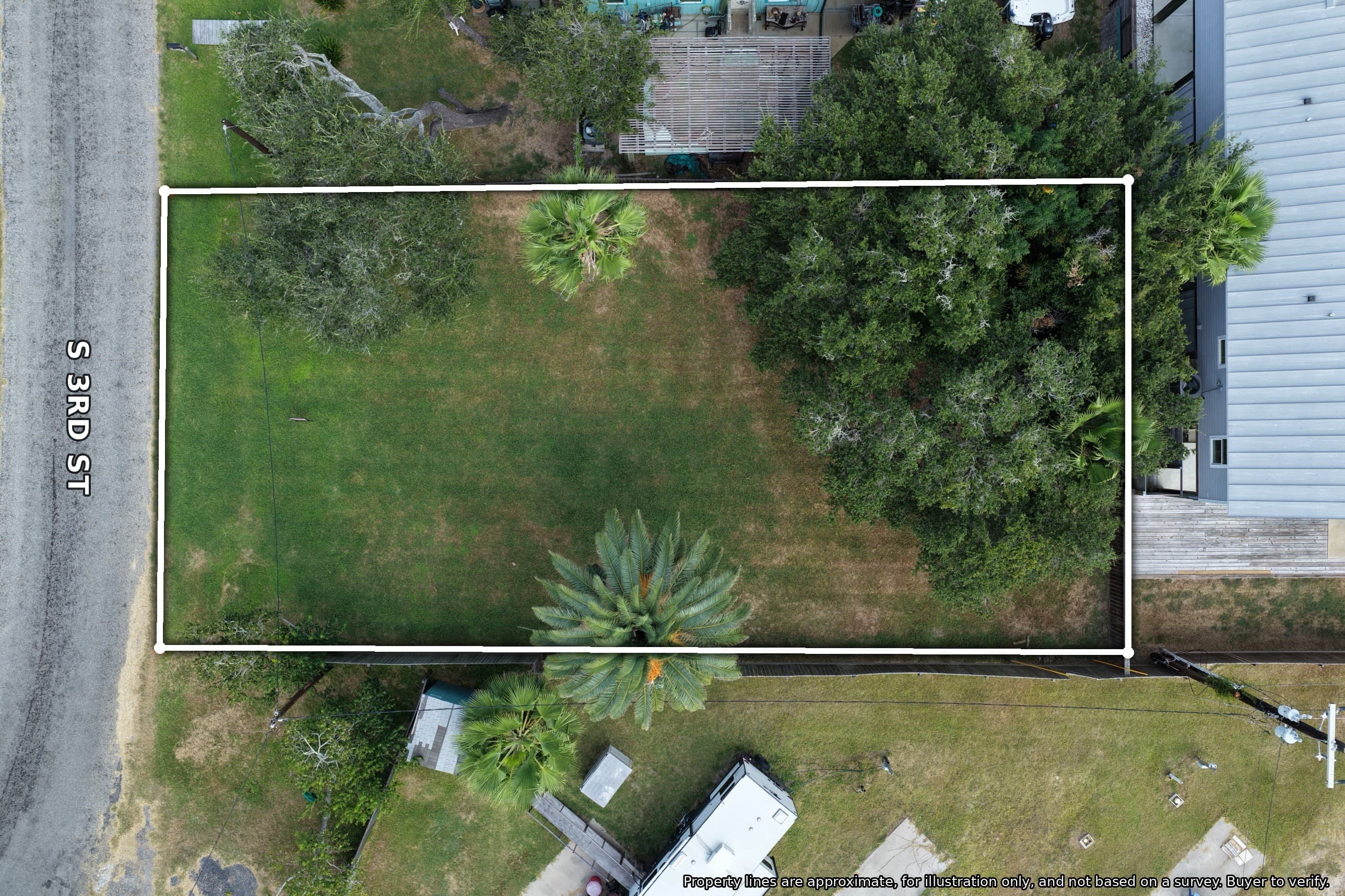 Aerial view of a rectangular grassy lot outlined in white, featuring palm and leafy trees.