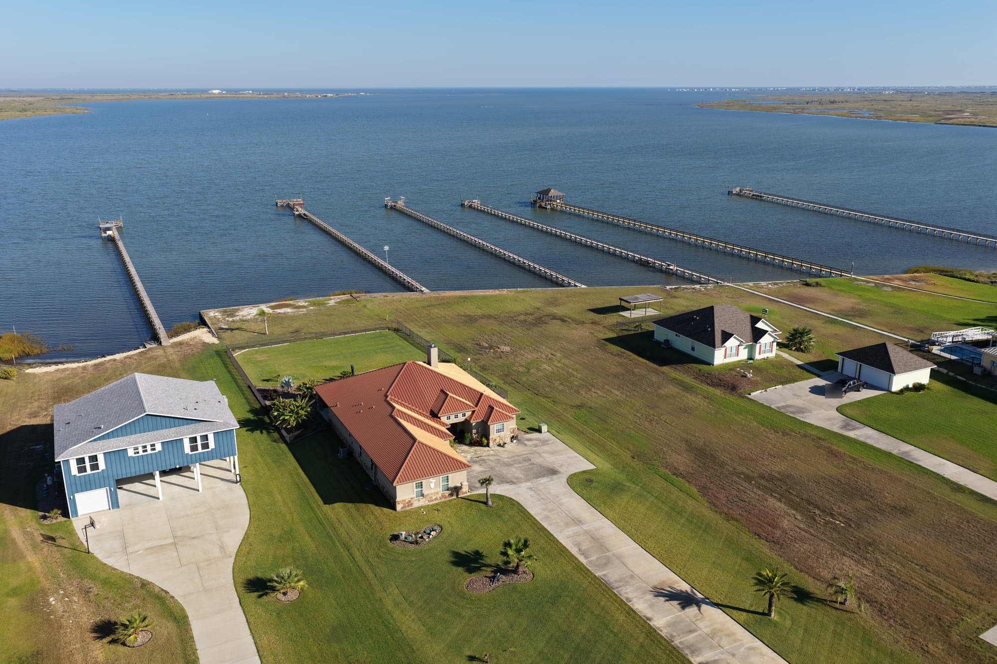Aerial view of waterfront homes with long wooden piers extending into a wide blue bay.