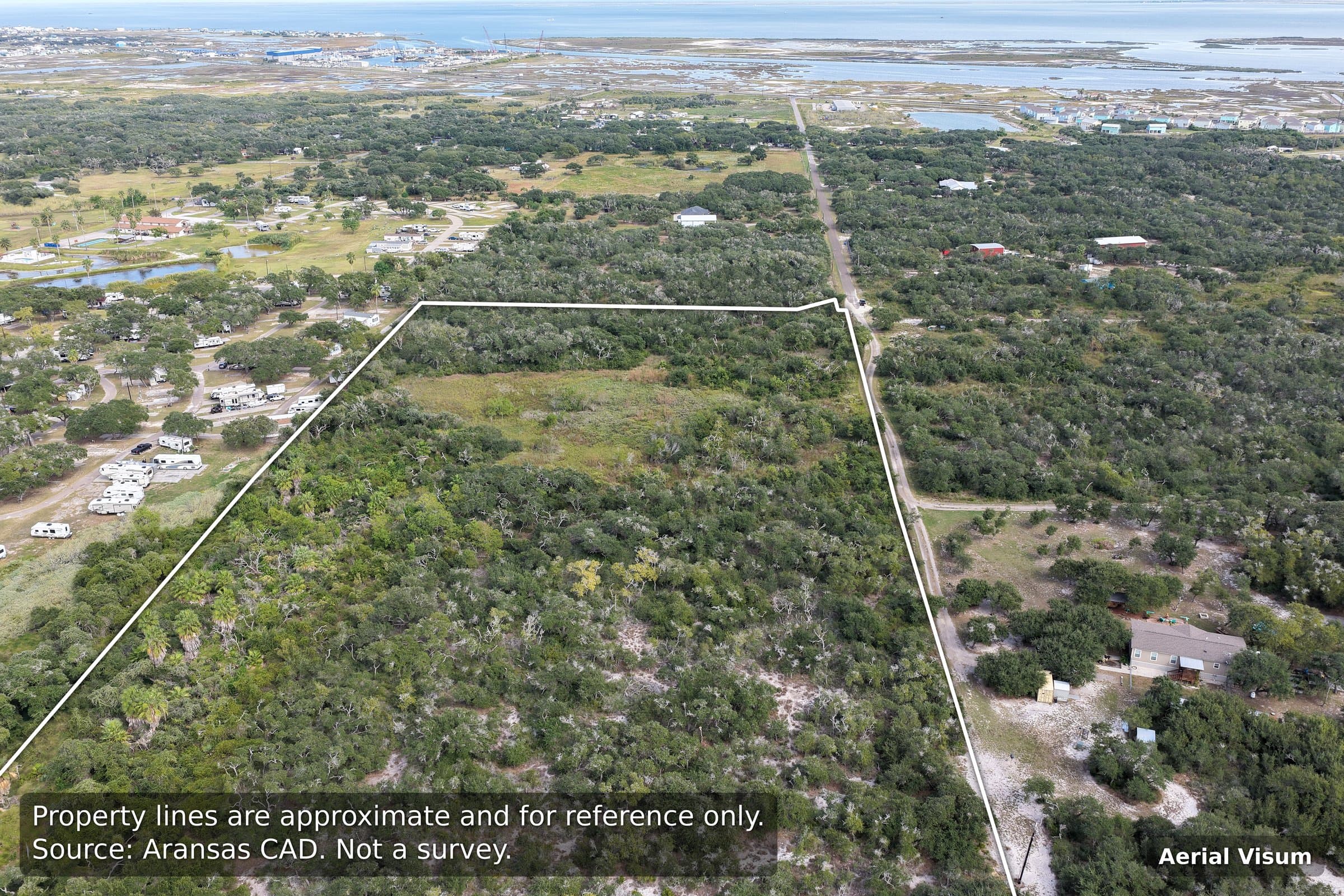 Aerial view of a large wooded property outlined in white, situated near a coastal bay.