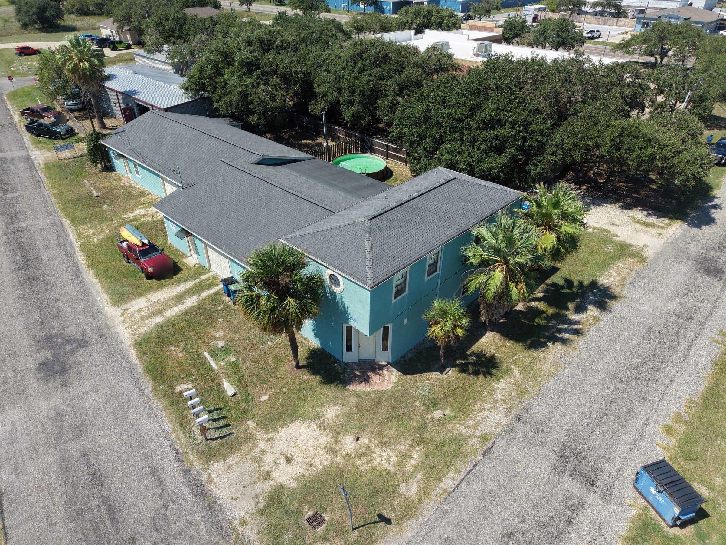 Aerial view of a light blue building with a dark grey roof and palm trees.