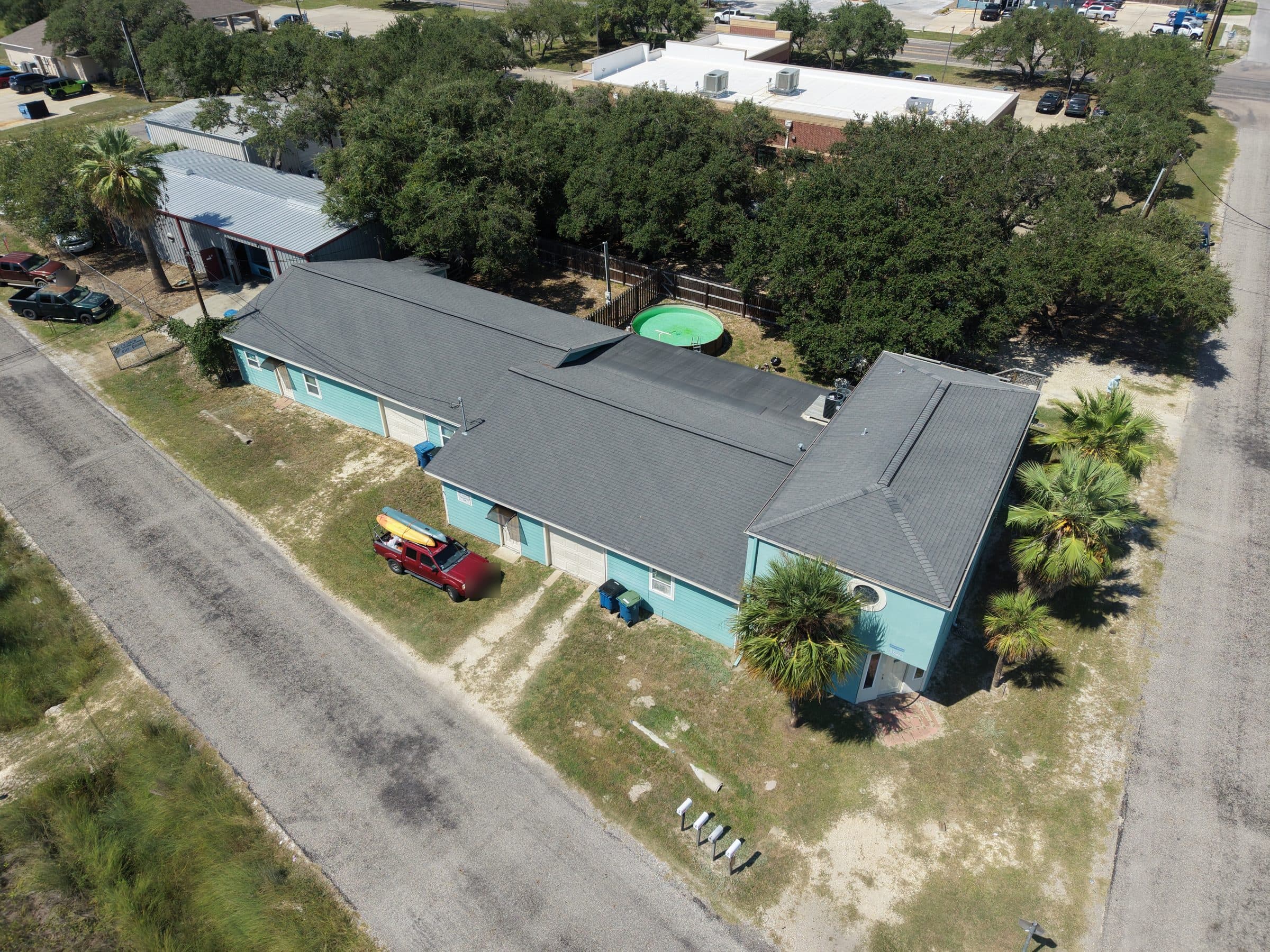 Aerial view of a light blue building with a red truck and a backyard pool.