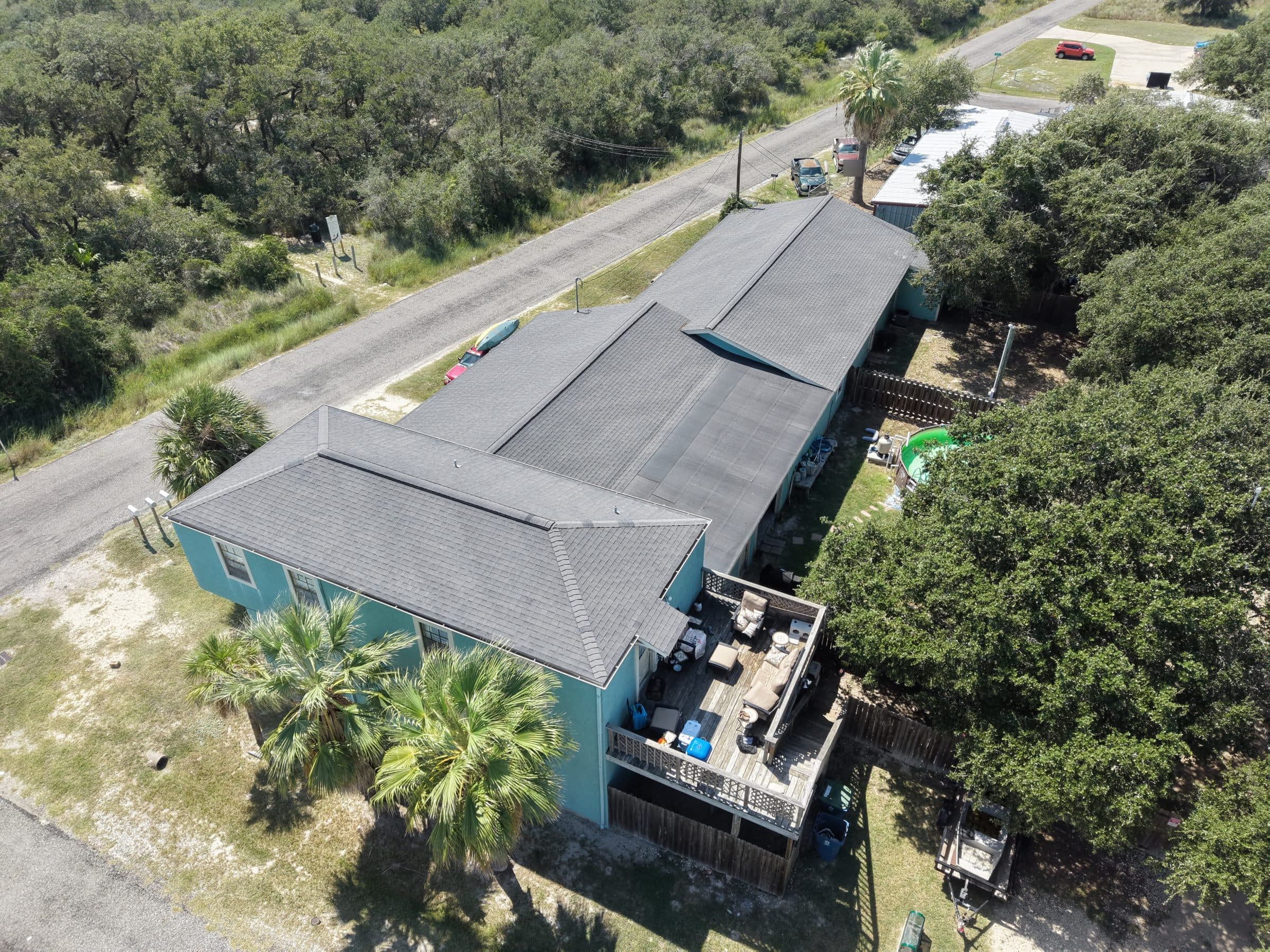 Aerial view of a long teal house with a dark grey roof and wooden balcony deck.