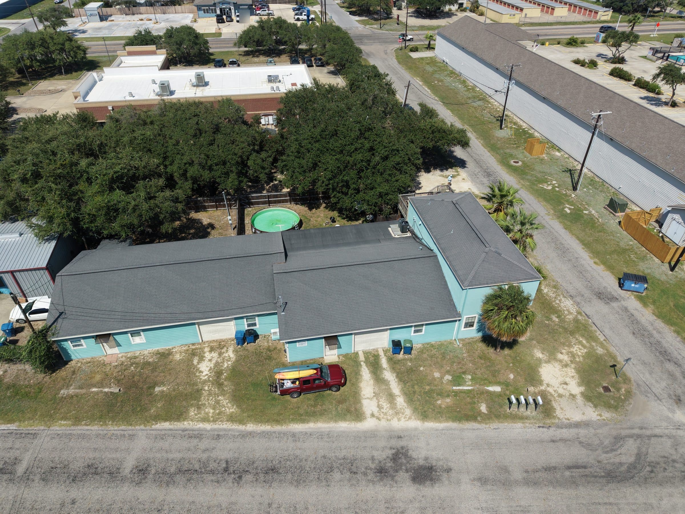 Aerial view of a light blue building with a red truck and kayaks parked outside.