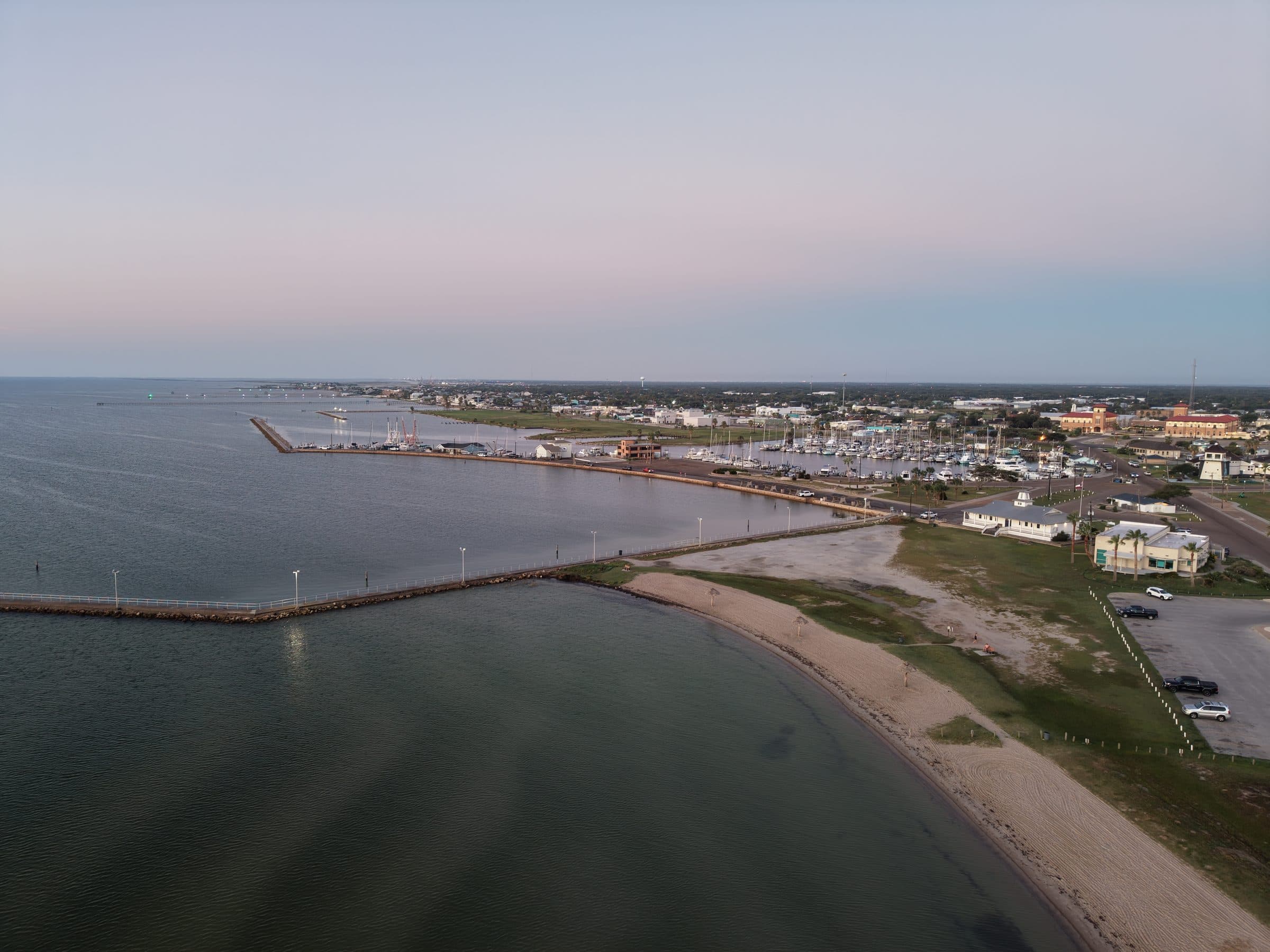 Aerial view of a coastal town at dusk with a long pier, beach, and marina.