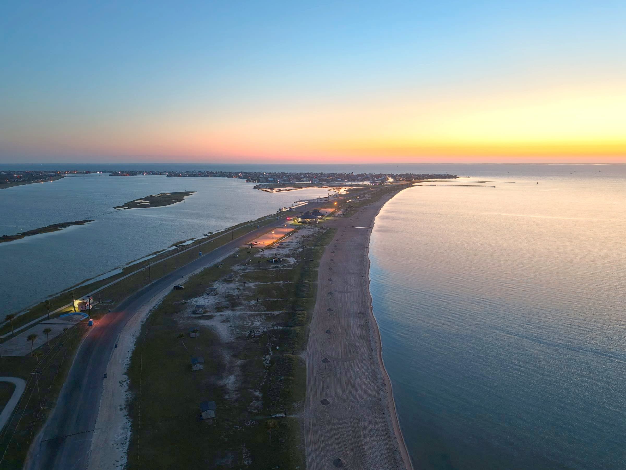Sunset aerial view of a narrow beach peninsula between two calm bodies of water.