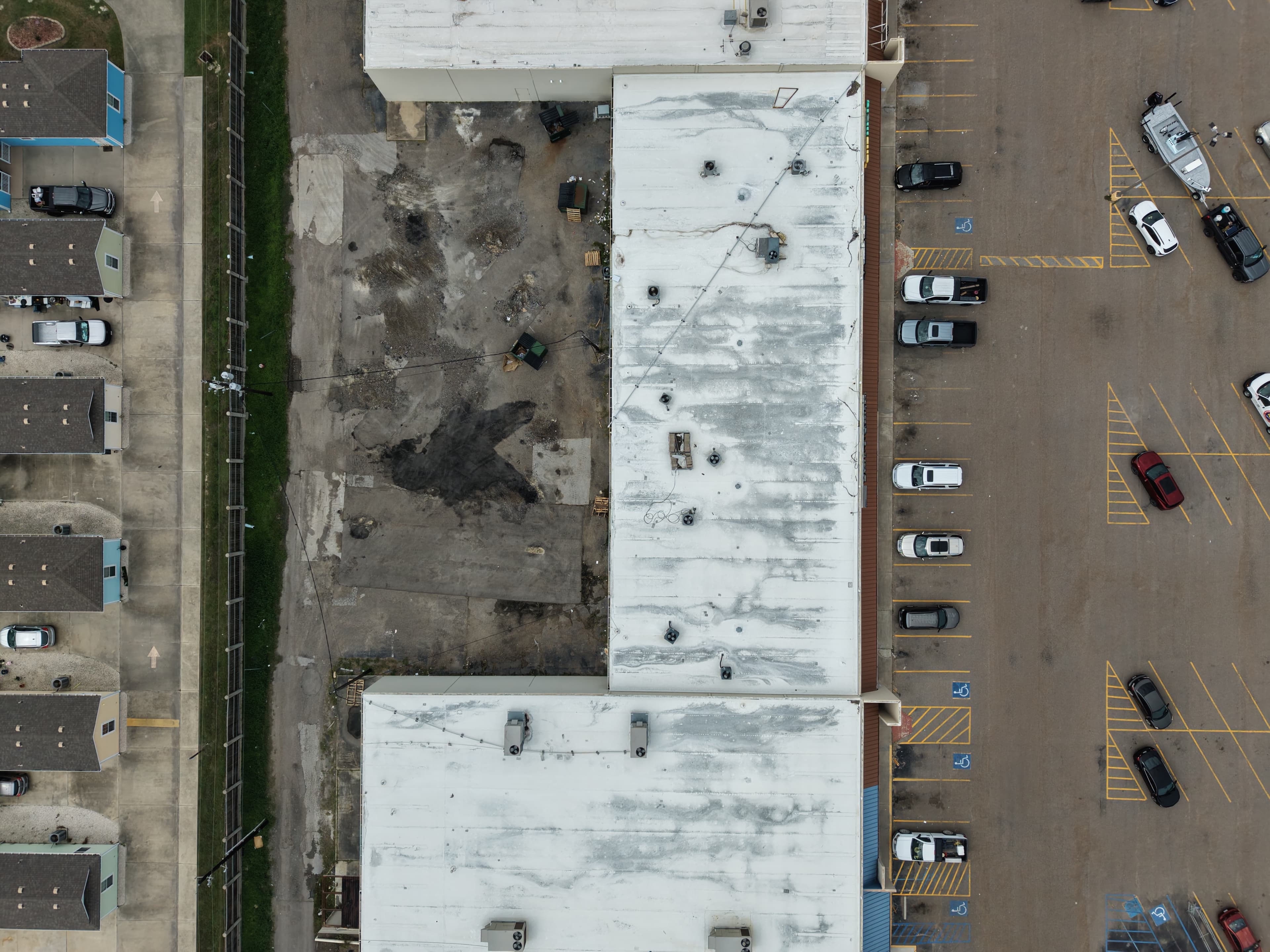 Top-down aerial view of a white commercial building, parking lot, and adjacent residential neighborhood.