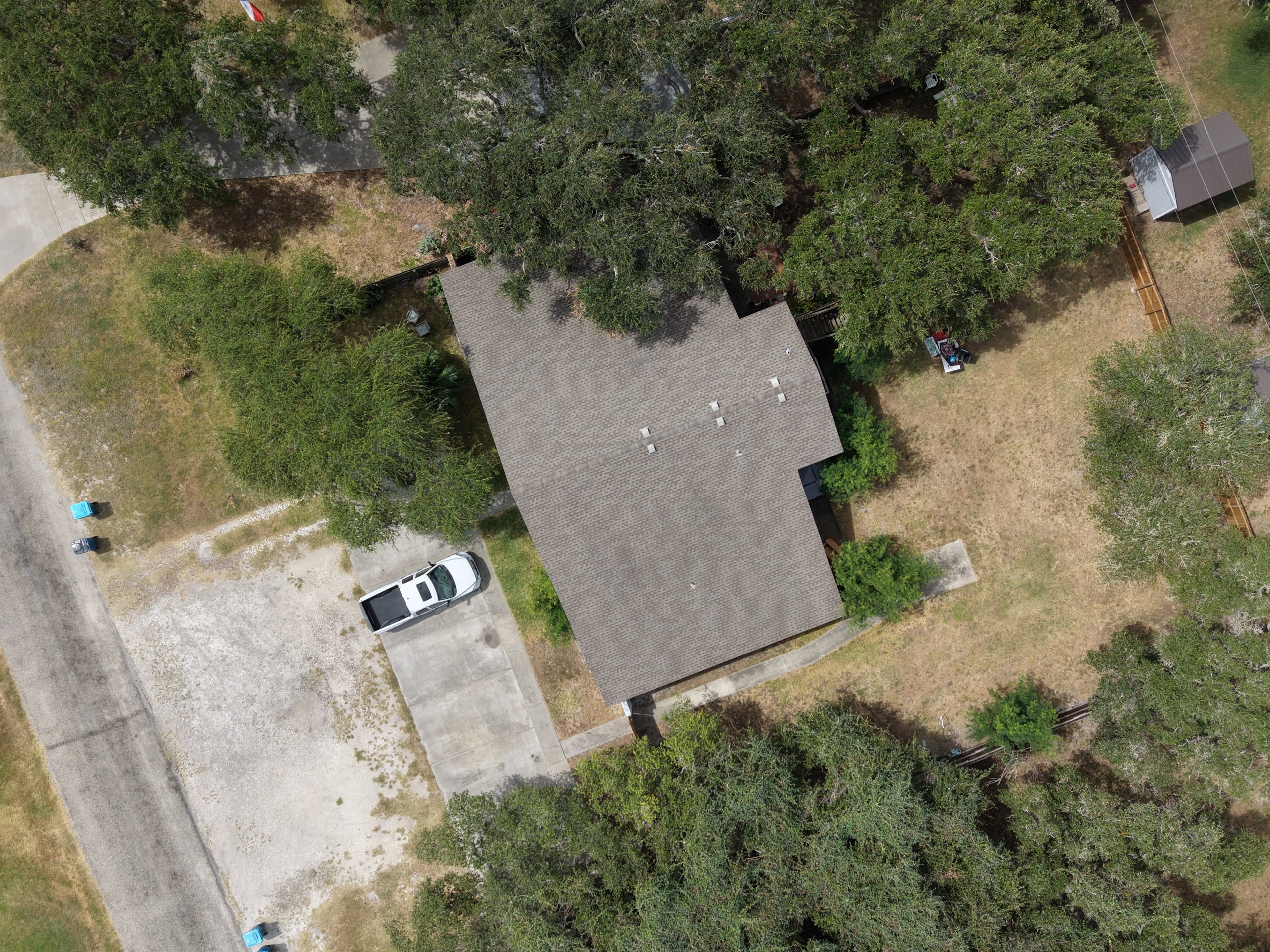Top-down view of a house with grey shingles, white pickup truck, and surrounding green trees.